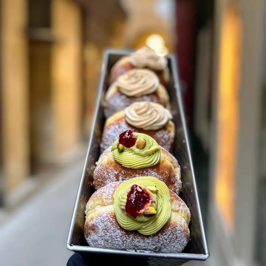 Eine Reihe Krapfen mit Pistaziencreme und Himbeere in einer Backform, im Hintergrund die Passage